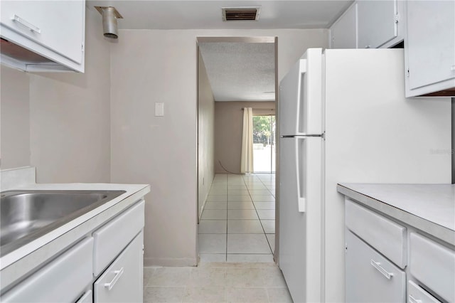 kitchen with light countertops, freestanding refrigerator, white cabinets, visible vents, and a sink