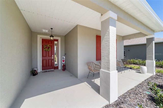 property entrance featuring stucco siding, visible vents, and covered porch