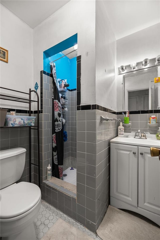 bathroom with toilet, tiled shower, wainscoting, and tile walls