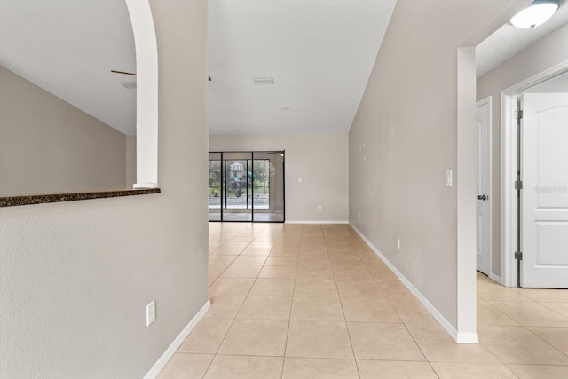 hallway with arched walkways, light tile patterned floors, and baseboards