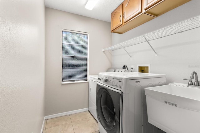 washroom with light tile patterned floors, independent washer and dryer, a sink, baseboards, and cabinet space
