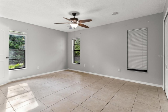 empty room with light tile patterned flooring, baseboards, a textured ceiling, and ceiling fan