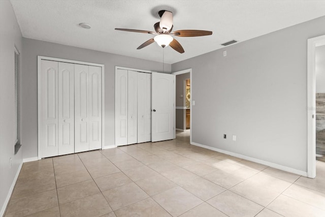 unfurnished bedroom featuring light tile patterned floors, visible vents, baseboards, and multiple closets