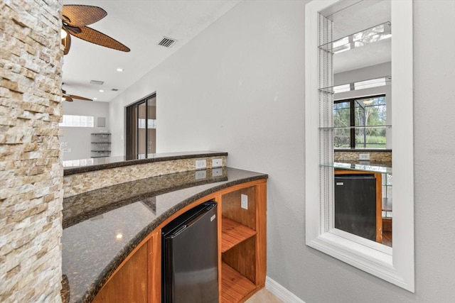 kitchen featuring dark stone countertops, visible vents, ceiling fan, brown cabinetry, and fridge