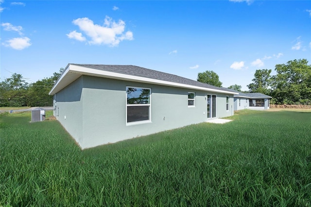 back of house featuring a lawn, central AC, and stucco siding