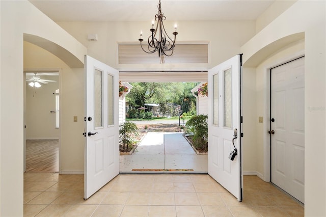 foyer entrance with arched walkways, ceiling fan with notable chandelier, light tile patterned flooring, and baseboards