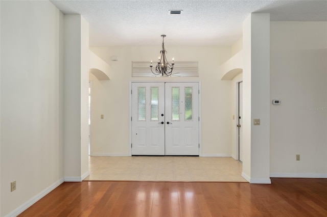 entrance foyer featuring visible vents, baseboards, arched walkways, an inviting chandelier, and wood finished floors
