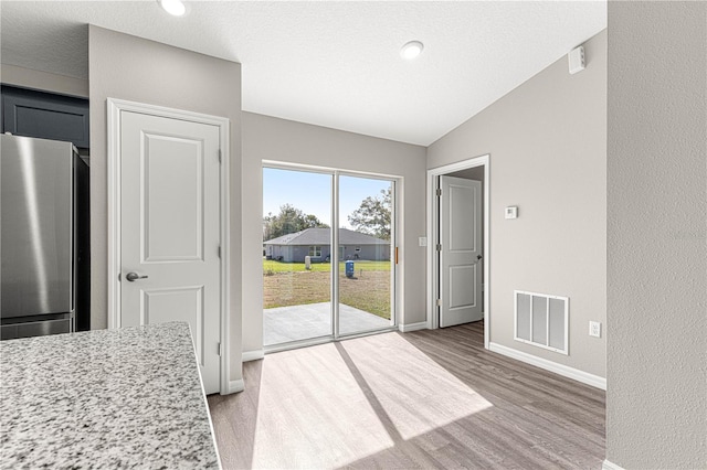 unfurnished dining area featuring visible vents, baseboards, light wood finished floors, and vaulted ceiling