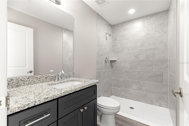 full bathroom with visible vents, toilet, tiled shower, and vanity