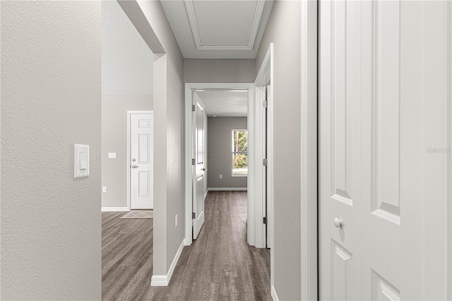 hallway featuring wood finished floors, a textured wall, and baseboards