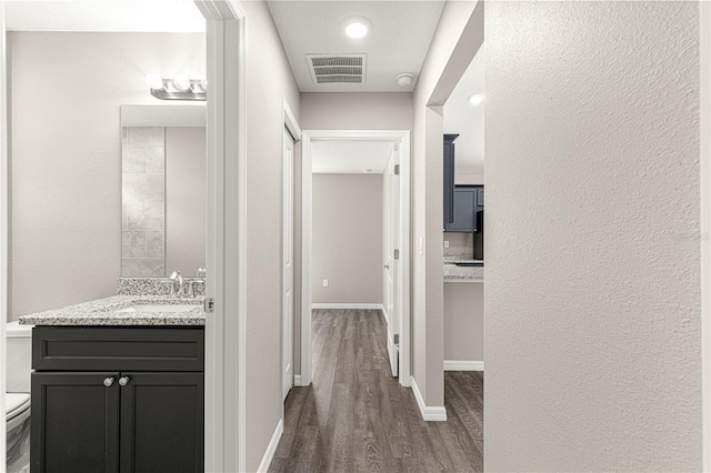 hall featuring visible vents, baseboards, a sink, and wood finished floors