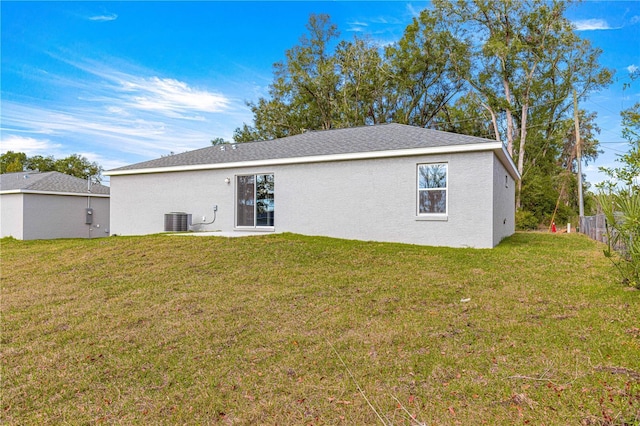 back of property featuring central AC, a lawn, and stucco siding