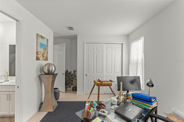 office space featuring light wood-type flooring, visible vents, baseboards, and a textured ceiling
