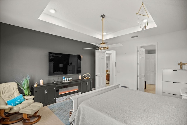 bedroom featuring a tray ceiling, a glass covered fireplace, visible vents, and recessed lighting