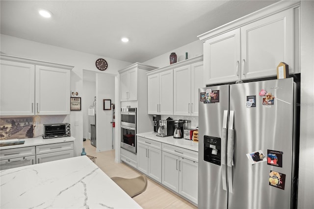 kitchen with decorative backsplash, appliances with stainless steel finishes, a toaster, and light stone counters