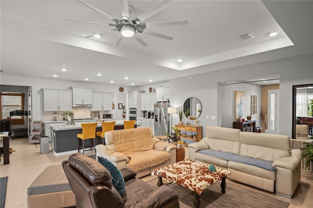 living area with a raised ceiling, ceiling fan, visible vents, and recessed lighting