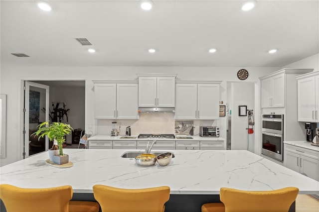 kitchen featuring a sink, under cabinet range hood, a breakfast bar area, appliances with stainless steel finishes, and white cabinetry