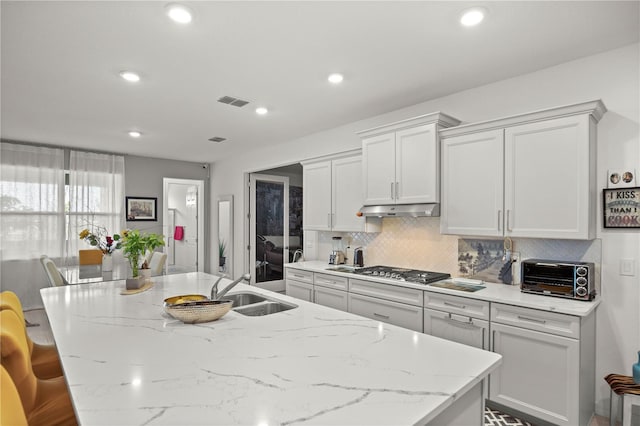 kitchen featuring tasteful backsplash, a sink, an island with sink, a toaster, and under cabinet range hood