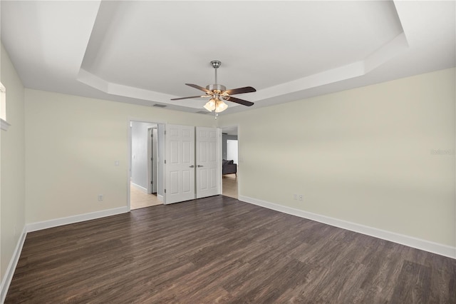 unfurnished bedroom featuring baseboards, a raised ceiling, ceiling fan, and dark wood-style floors