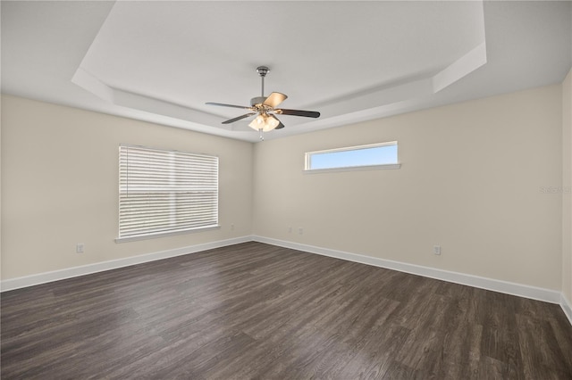empty room with baseboards, dark wood-type flooring, a tray ceiling, and a ceiling fan