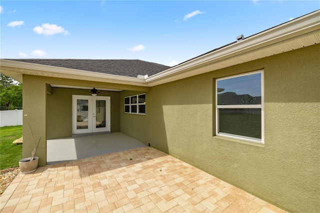 view of exterior entry featuring a patio, roof with shingles, stucco siding, french doors, and fence