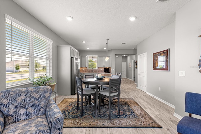 dining space featuring baseboards, light wood-style floors, a textured ceiling, and recessed lighting