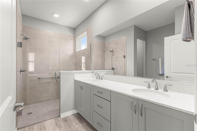 full bath featuring double vanity, a shower stall, wood finished floors, and a sink