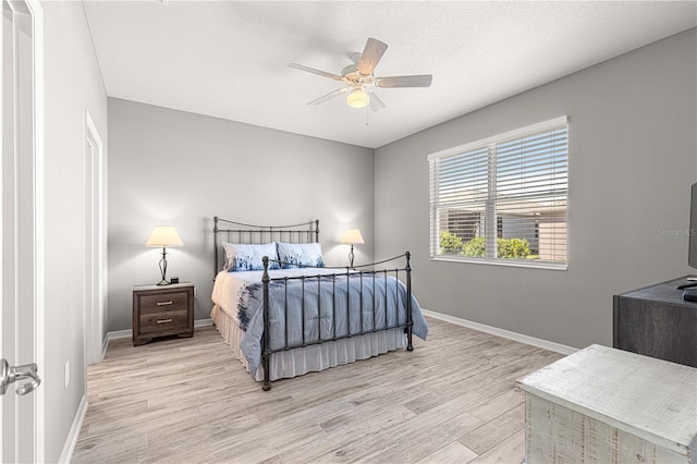 bedroom with light wood-style flooring, a ceiling fan, and baseboards