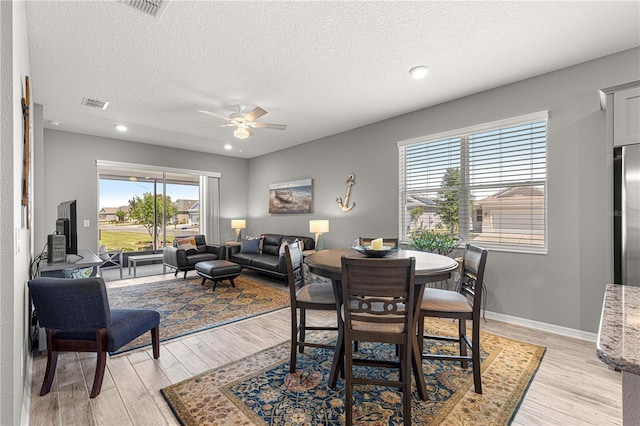 dining area featuring a textured ceiling, light wood-style floors, visible vents, and ceiling fan