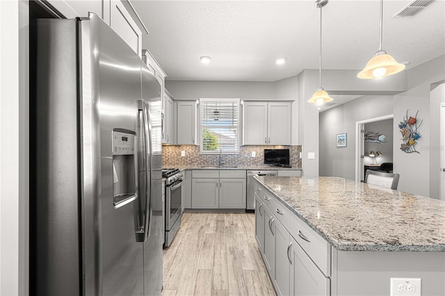 kitchen with stainless steel appliances, visible vents, a sink, light wood-style floors, and a center island