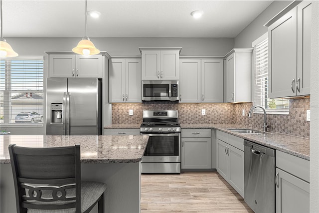 kitchen featuring light stone counters, a sink, stainless steel appliances, light wood-style flooring, and gray cabinetry