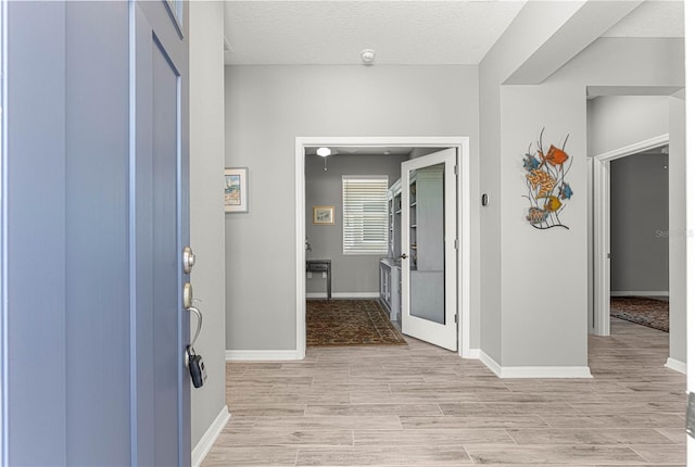 entrance foyer featuring light wood-style flooring, baseboards, and a textured ceiling