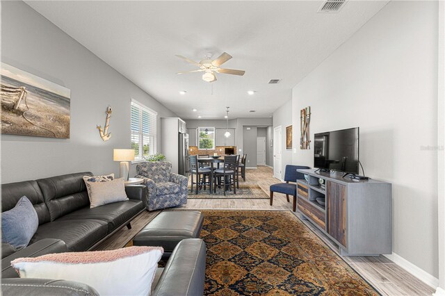 living area featuring light wood-style floors, visible vents, baseboards, and ceiling fan