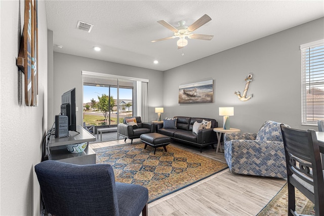 living area with ceiling fan, wood finished floors, visible vents, and a textured ceiling
