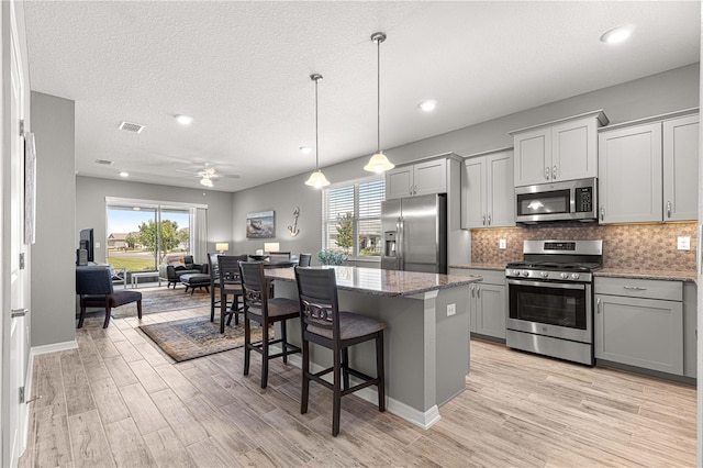 kitchen featuring gray cabinets, appliances with stainless steel finishes, light stone countertops, and light wood-style floors