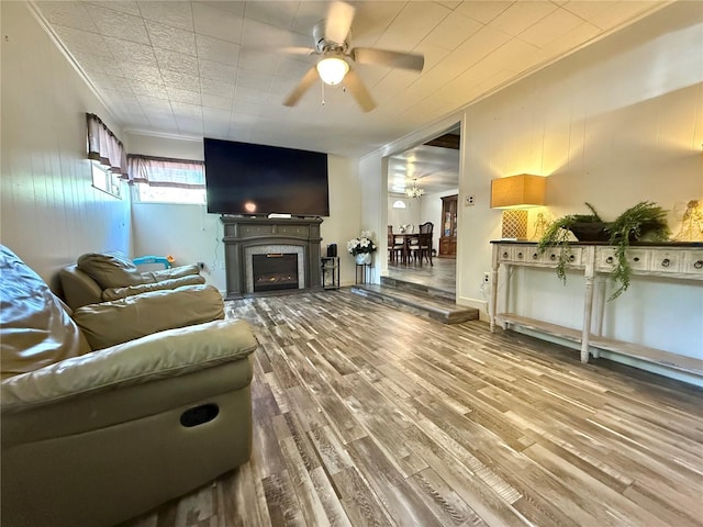 living room featuring a fireplace, a ceiling fan, ornamental molding, and wood finished floors