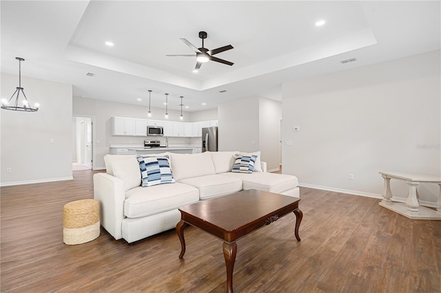 living area with a raised ceiling, ceiling fan, wood finished floors, a chandelier, and recessed lighting