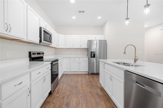 kitchen featuring stainless steel appliances, a sink, dark wood-type flooring, light countertops, and white cabinetry