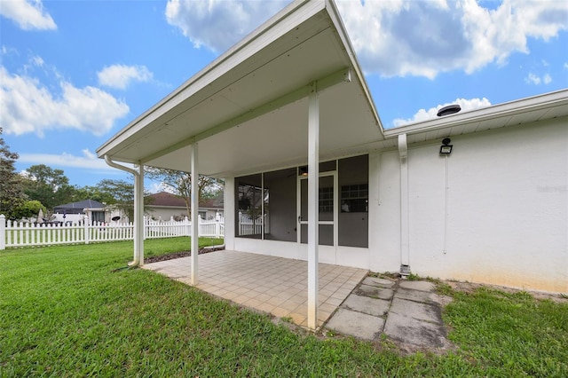 exterior space with fence, a yard, a patio, stucco siding, and a sunroom