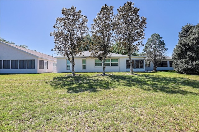 back of property with a sunroom, a lawn, and stucco siding