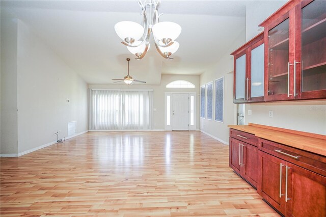 interior space featuring reddish brown cabinets, vaulted ceiling, ceiling fan with notable chandelier, baseboards, and light wood-type flooring