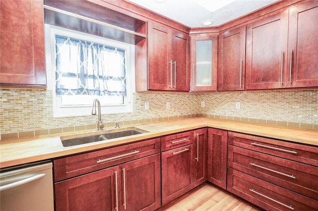 kitchen with reddish brown cabinets, light wood-type flooring, stainless steel dishwasher, and a sink