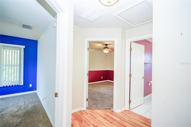 hallway featuring baseboards, visible vents, and light colored carpet