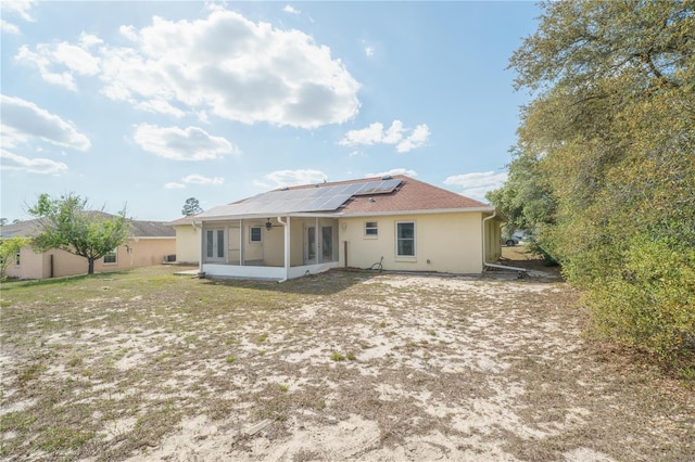 rear view of house with stucco siding, roof mounted solar panels, and a sunroom