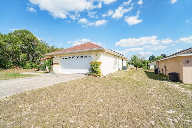 view of side of home featuring concrete driveway, an attached garage, stucco siding, a yard, and central AC unit