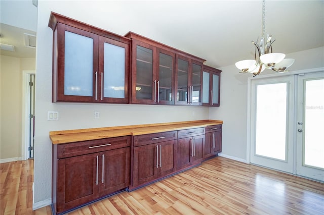 kitchen featuring a chandelier, glass insert cabinets, light wood-type flooring, decorative light fixtures, and french doors