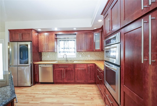 kitchen featuring reddish brown cabinets, decorative backsplash, stainless steel appliances, light wood finished floors, and a sink