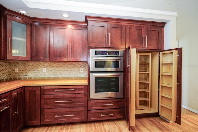 kitchen with stainless steel double oven, dark brown cabinets, decorative backsplash, and light wood-type flooring
