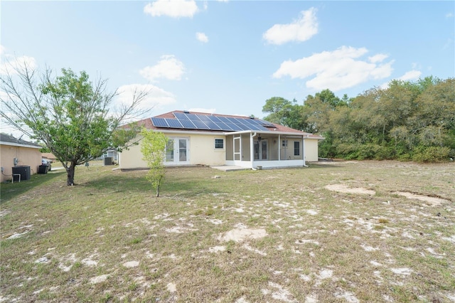 back of property featuring cooling unit, stucco siding, solar panels, a lawn, and a sunroom