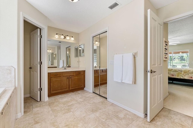 full bath featuring a textured ceiling, vanity, tiled tub, ensuite bath, and visible vents